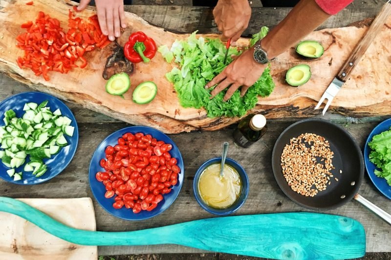 Fresh ingredients being prepared on a rustic wooden table, showcasing vibrant vegetables and hands at work.